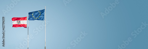 Photography Two flags of EU and Austria standing in wind together at blue sky gradient backg