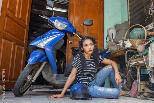 A young woman is sitting by a motorcycle parked in front of the entrance to a house