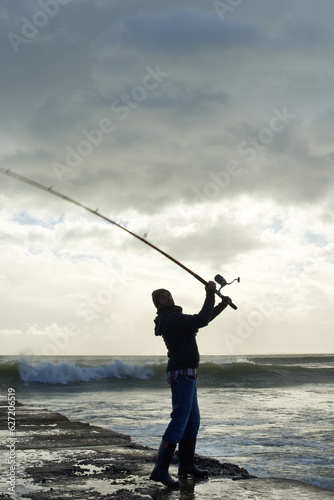 Taking his time for the big catch. Shot of a solo fisherman fishing off a pier at the ocean.