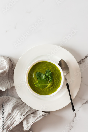 Healthy breakfasts, green broccoli and spinach cream soup in a white bowl on a marble background with a gray napkin, top view