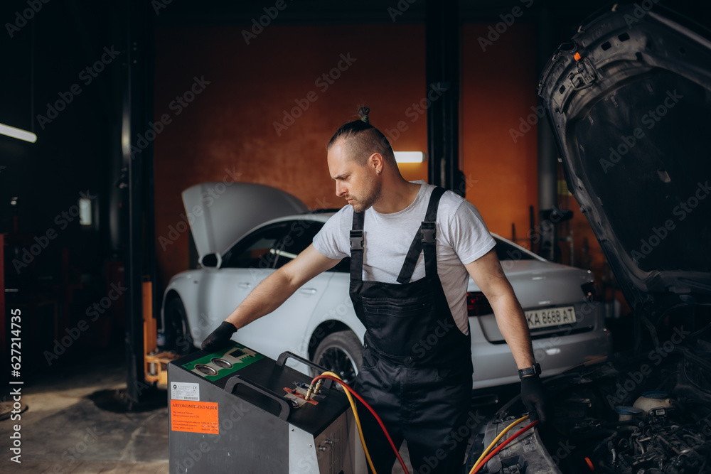 Car mechanic with manometer to fill the gas in the car air conditioning compressor. Service of checking the car air conditioner. Refrigerant recharge system. Car mechanic with manometer to fill the gas in the car air conditioning compressor. Service of checking the car air conditioner. Refrigerant recharge system.