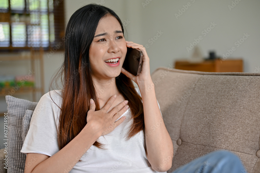 A cheerful Asian woman having a casual phone call with her friend while sitting on the sofa A cheerful Asian woman having a casual phone call with her friend while sitting on the sofa