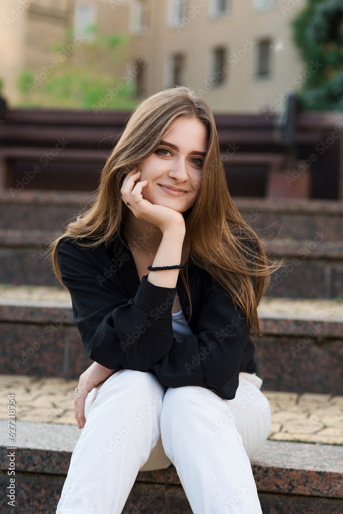 Portrait of a young and attractive happy girl sitting on the steps on a summer day in casual clothes. Portrait of a young and attractive happy girl sitting on the steps on a summer day in casual clothes.