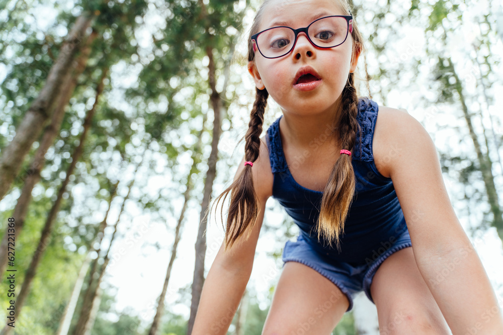 Low angle view portrait of a cute little girl with special needs at the forest outdoor summer vacation. Cute caucasian little girl playing on a playground and having fun in park. Low angle view portrait of a cute little girl with special needs at the forest outdoor summer vacation. Cute caucasian little girl playing on a playground and having fun in park.
