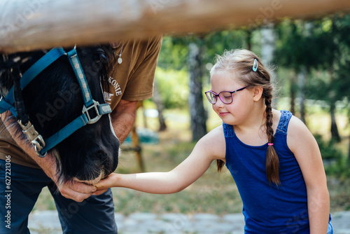 Quadro su tela Little brown haired girl feeding and stroking a pony horse outdoor