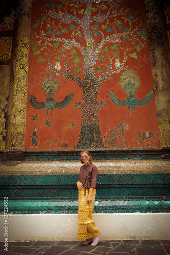 woman tourist standing infront of beautiful art on wat xiang thong sculpture ,wat xiangthong is one of most important visitor attraction at luangprabang world heritage site of unesco in northern laos photo
