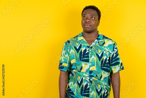 Young latin man wearing hawaiian shirt over yellow background looking aside into empty space thoughtful