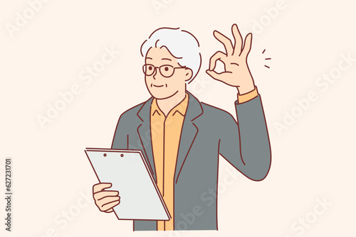 Elderly businessman showing OK gesture and holding clipboard checking work of subordinates