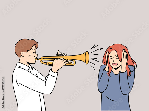 Man plays trumpet near woman covering ears, for concept trumpeter lack musical talent. Guy who wants to become professional musician learns to play compositions on trumpet and interferes with others