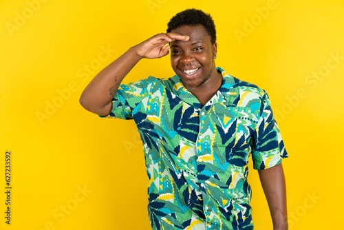 Wallpaper Mural Young latin man wearing hawaiian shirt over yellow background very happy and smiling looking far away with hand over head. Searching concept. Torontodigital.ca