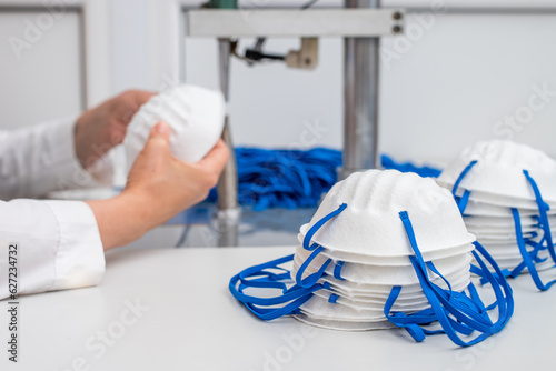 The girl works in a factory for the production of medical masks with nanofibre and solder loops with ultrasound on a machine. Coronavirus and Covid-19 Protection.Close-up.