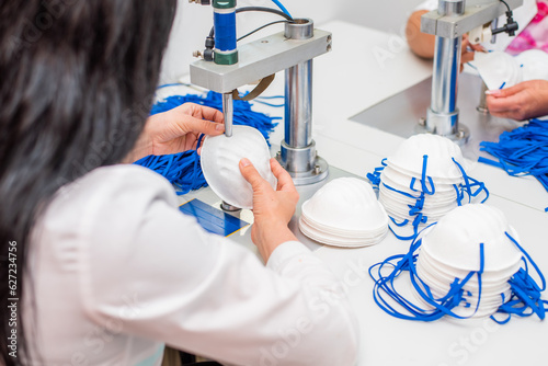 Women work at a machine for the manufacture of medical masks with nanofiber and solder loops to them with ultrasound. Coronovirus and Covid-19 Prevention photo