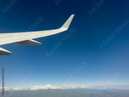 White wing from airplane window on sunny day. Great views of landscape. Aerial view of clouds through a plane window. Wing of airplane with blue sky and beauty clouds © Aleksei