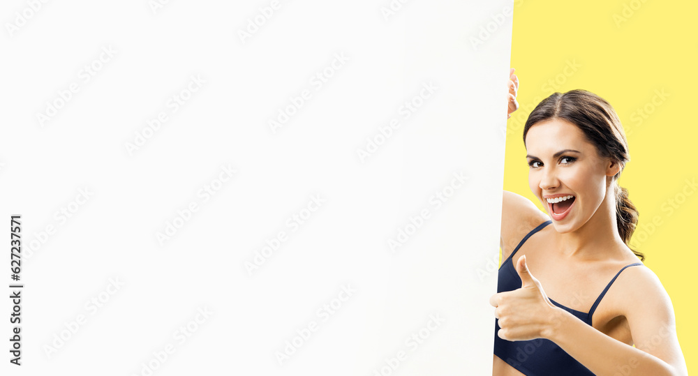 Photo of excited brunette woman in fitness wear showing thumb up, blank paper signboard with copy space free area. Fit girl with happy wide open mouth, peek out mock up white placard, on yellow color. Photo of excited brunette woman in fitness wear showing thumb up, blank paper signboard with copy space free area. Fit girl with happy wide open mouth, peek out mock up white placard, on yellow color.