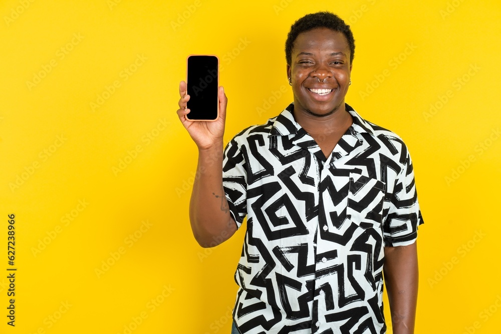Smiling Young latin man wearing printed shirt over yellow background Mock up copy space. Hold mobile phone with blank empty screen Smiling Young latin man wearing printed shirt over yellow background Mock up copy space. Hold mobile phone with blank empty screen