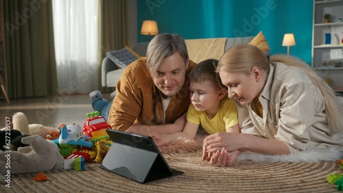 Young parents mother and father with their little kid spending time together watching tablet