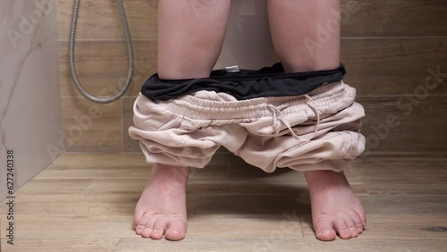 Barefoot woman pulls down pants for doing needs in toilet in modern bathroom of apartment. Concept of daily routine. Intimate process