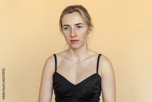 Portrait of the thoughtful upset woman standing over beige background, lost in thoughts. Pensive unhappy girl feeling lonely and depressed, thinking about relationship or personal problems