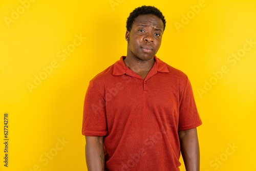 Displeased Young latin man wearing red t-shirt over yellow background frowns face feels unhappy has some problems. Negative emotions and feelings concept photo