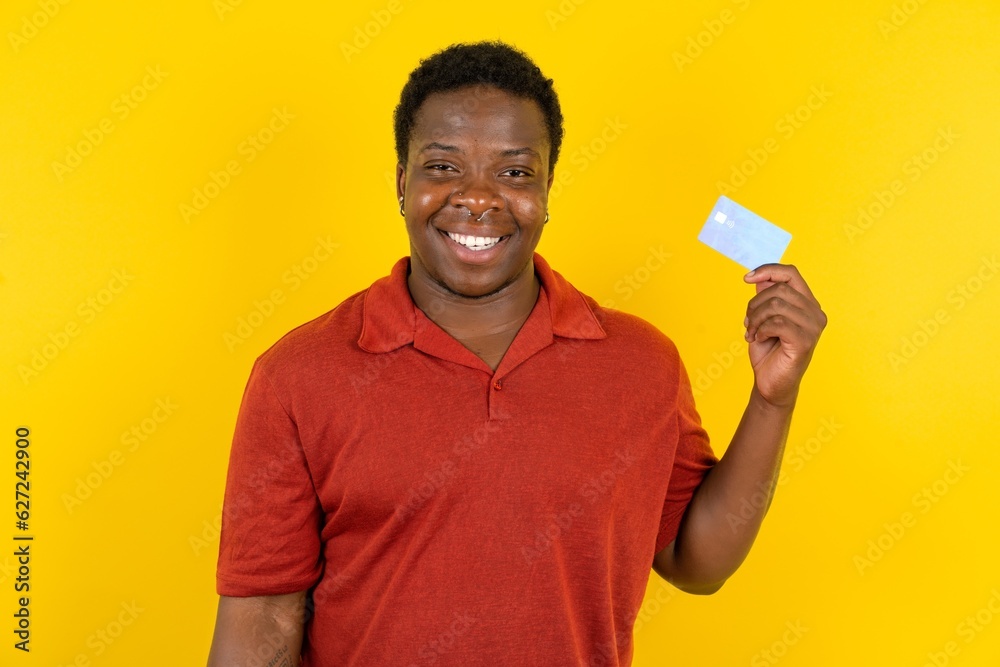Photo of happy cheerful smiling positive Young latin man wearing red t-shirt over yellow background recommend credit card Photo of happy cheerful smiling positive Young latin man wearing red t-shirt over yellow background recommend credit card