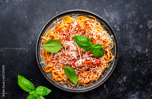 Spaghetti bolognese or pasta with minced meat in tomato sauce with green basil sprinkled with grated parmesan cheese, dark table, top view