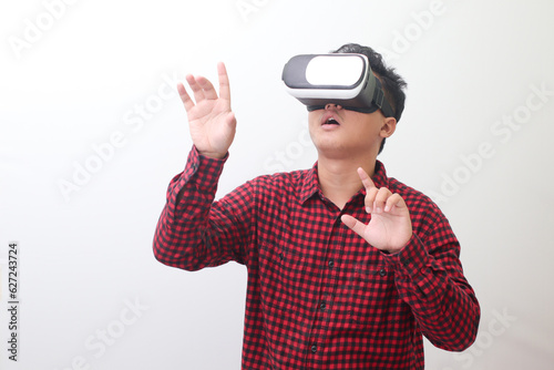 Portrait of Asian man in red plaid shirt using Virtual Reality  VR  glasses and protecting himself by spreading his arms from something big falling from above. Isolated image on white background