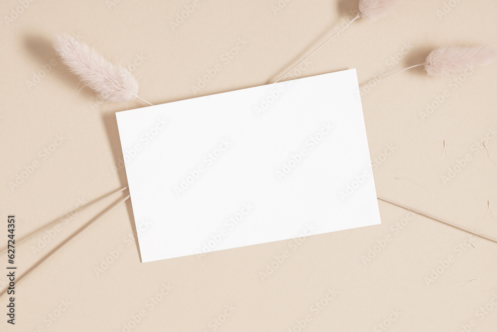 White paper empty blank, dry flowers, dried branch on beige background. Invitation card mockup on beige table. Flat lay, top view, copy space, mockup White paper empty blank, dry flowers, dried branch on beige background. Invitation card mockup on beige table. Flat lay, top view, copy space, mockup