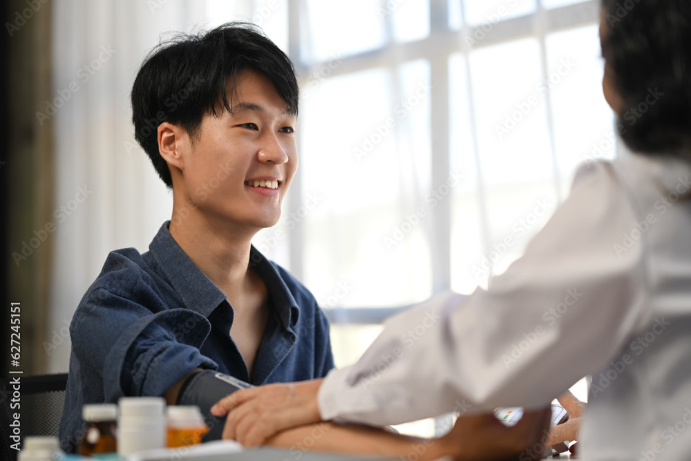 Asian man patient sitting in examining room having blood pressure checked by doctor Asian man patient sitting in examining room having blood pressure checked by doctor