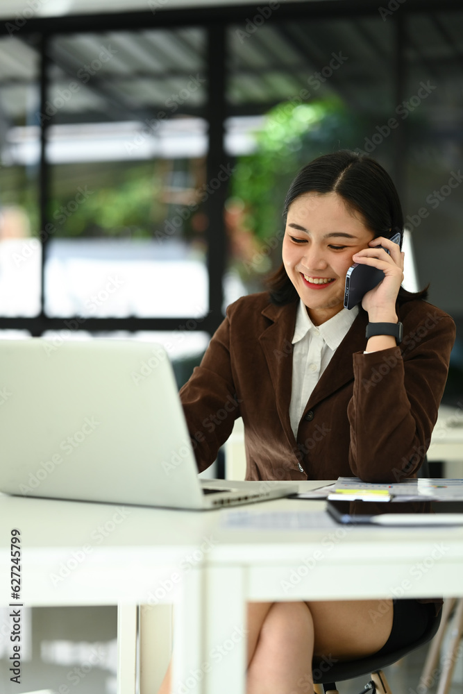 Friendly female financial advisor using laptop and consulting client distantly by mobile phone call