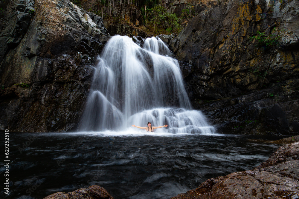 girl in bikini swimming in a rock pool under large tropical waterfall - jourama falls in paluma range national park near townsville, tropical north queensland, australia girl in bikini swimming in a rock pool under large tropical waterfall - jourama falls in paluma range national park near townsville, tropical north queensland, australia
