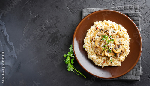A dish of Italian cuisine - risotto from rice and mushrooms in a brown plate on a black slate background. Top view. Flat lay. Copy space.