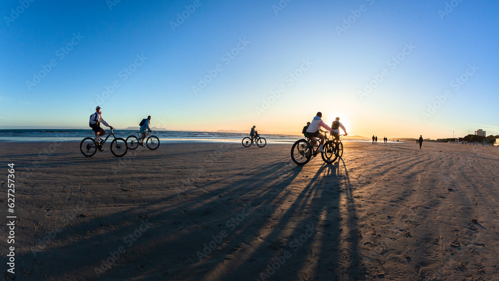 Beach Riders Cycling Sun Down Silhouettes Ocean Coastline Landscape. Beach Riders Cycling Sun Down Silhouettes Ocean Coastline Landscape.