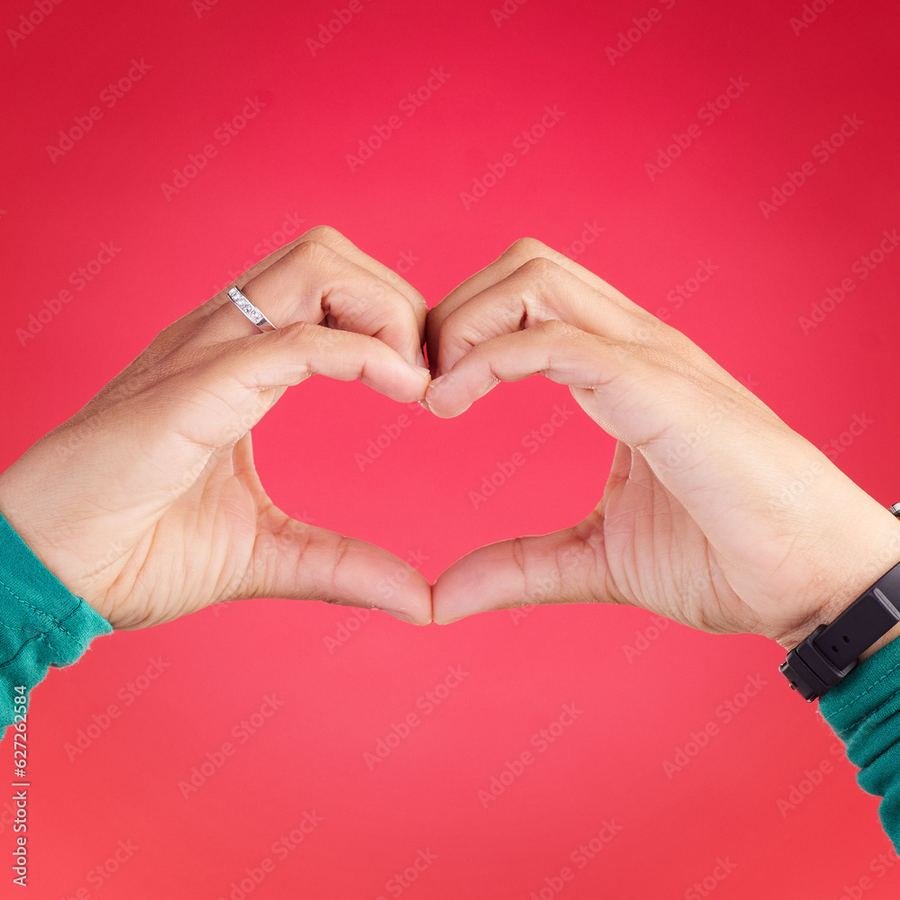 Fototapeta premium Closeup, person and heart hands for love, care or compassion against a red studio background. Hand together in loving emoji, shape or symbol for romantic gesture, icon or valentines day