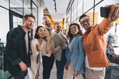 Group of multiethnic colleagues talking selfie in office corridor together