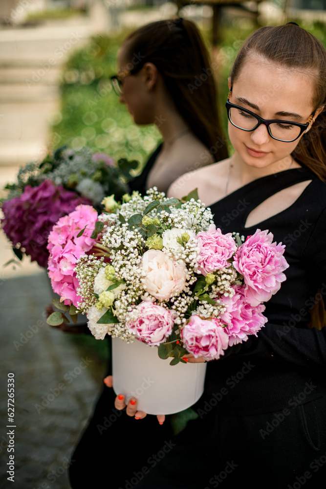 Fototapeta premium Mixed flower composition with hydrangea, peonies, carnations in white hat box in young woman's hands