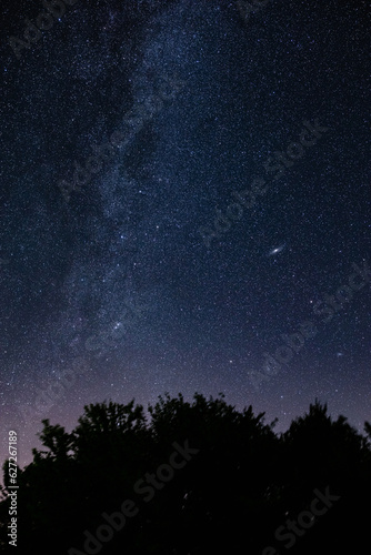Milky way stars and countryside silhouettes photographed with wide angle lens.