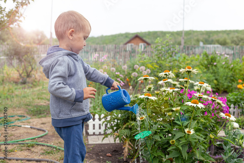 Cute little boy watering flowers with a baby watering can in the garden. Summer outdoor activity for children.