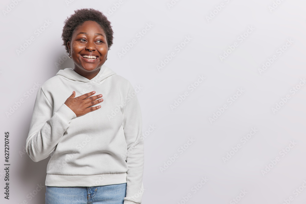 Εκτύπωση καμβά Horizontal shot of cheerful dark skinned woman keeps hand on chest feels gratitu
