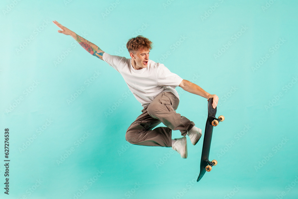 Ταπετσαρία young crazy guy rides skateboard and jumps on blue isolated background, hipster