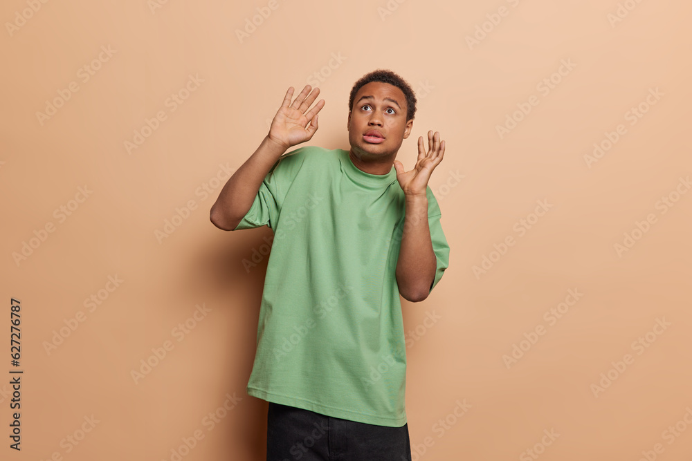 People negative emotions concept. Horizontal waist up of young fit frightened African man as if seeing something unusual or unexpected holding hands raised isolated in centre on beige background People negative emotions concept. Horizontal waist up of young fit frightened African man as if seeing something unusual or unexpected holding hands raised isolated in centre on beige background