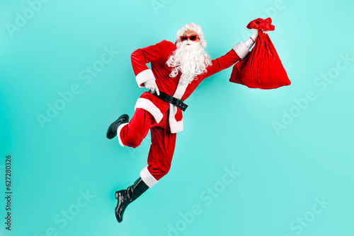 santa claus in suit with bag of gifts jumps and quickly runs in the air on blue isolated background © Богдан Маліцький