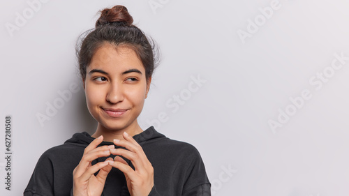 Cunning young woman with mischievous smirk and fingers steepled reveals devious idea brewing in her mind dressed in casual black hoodie isolated over white background copy space for your advertisement
