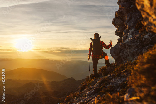 Billede på lærred man from behind with backpack, mountaineer, with trekking poles contemplating the sunset after reaching the peak of a mountain