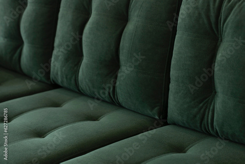 Soft vintage sofa in green velor with a quilted seat and a back of stitched cushions. Part of stylish furniture covered with plush fabric in emerald color close-up. photo