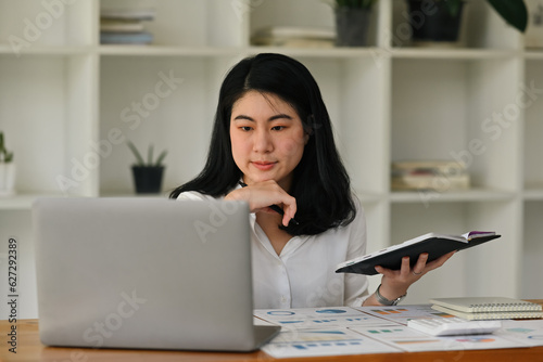 Portrait with Asian businesswoman working with laptop, Analyze graphs, diagrams and figures of financial document on office desk. © saltdium