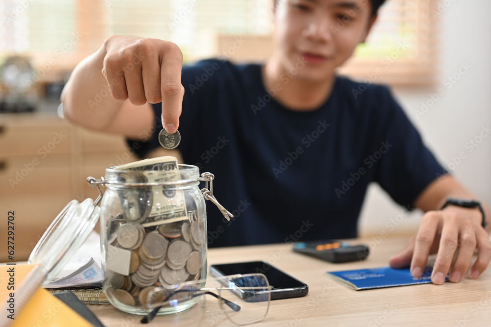 Φωτογραφία Cropped image of Young Asian man putting Thai currency coin in saving jar to save money purpose for investment or retirement