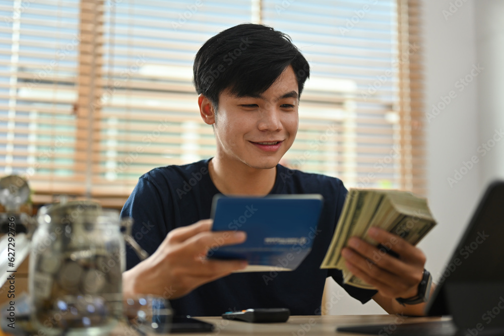 Φωτογραφία The young man looked happy after looking at the balance of his passbook, Concept of saving money for the future