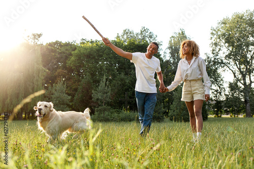 african american happy couple walk and run together with dog in park in summer