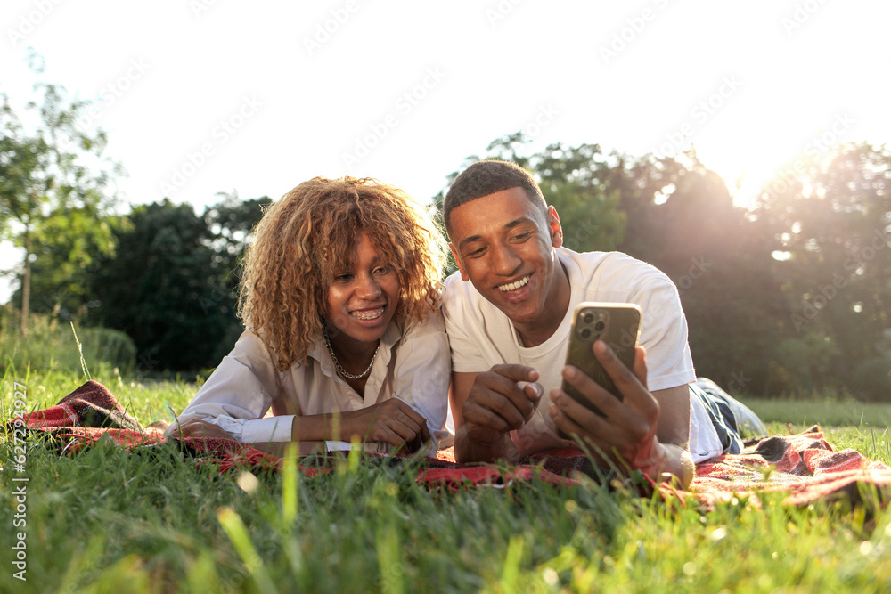 african american young couple lies in the park in the summer and uses smartphone african american young couple lies in the park in the summer and uses smartphone