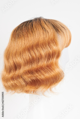 Natural looking ginger wig on white mannequin head. Medium length hair with wavy curls on the plastic wig holder isolated on white background, side view